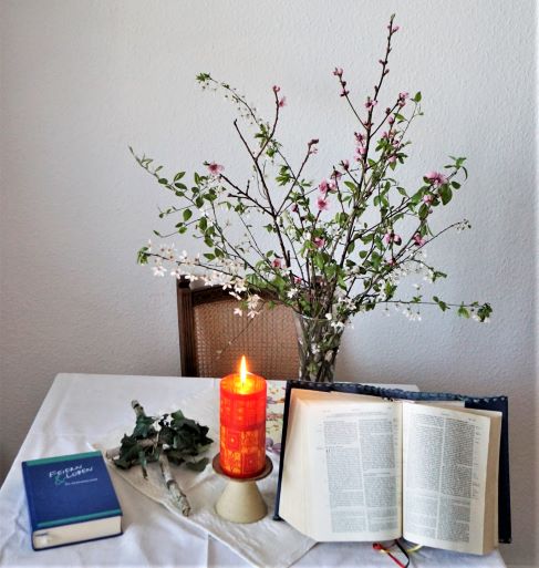 Bibel, Kerze, Gesangbuch und Blumenstrauß auf Tisch